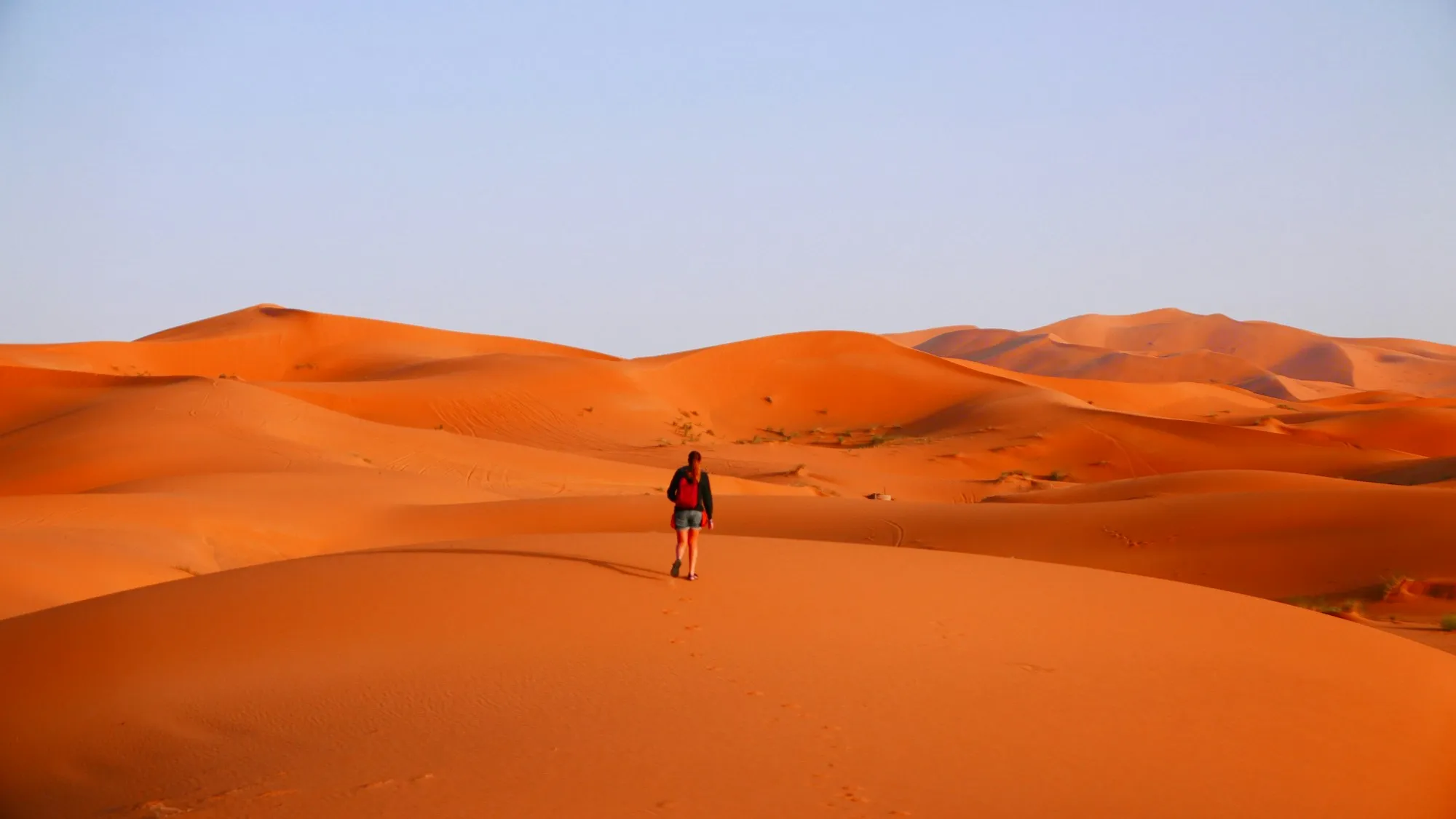 Una viajera con mochila caminando por las dunas del desierto