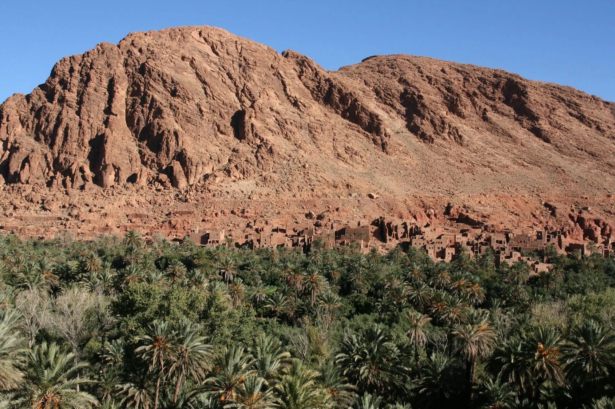 Pueblo de adobe y palmeral al pie de una gran montaña rocosa