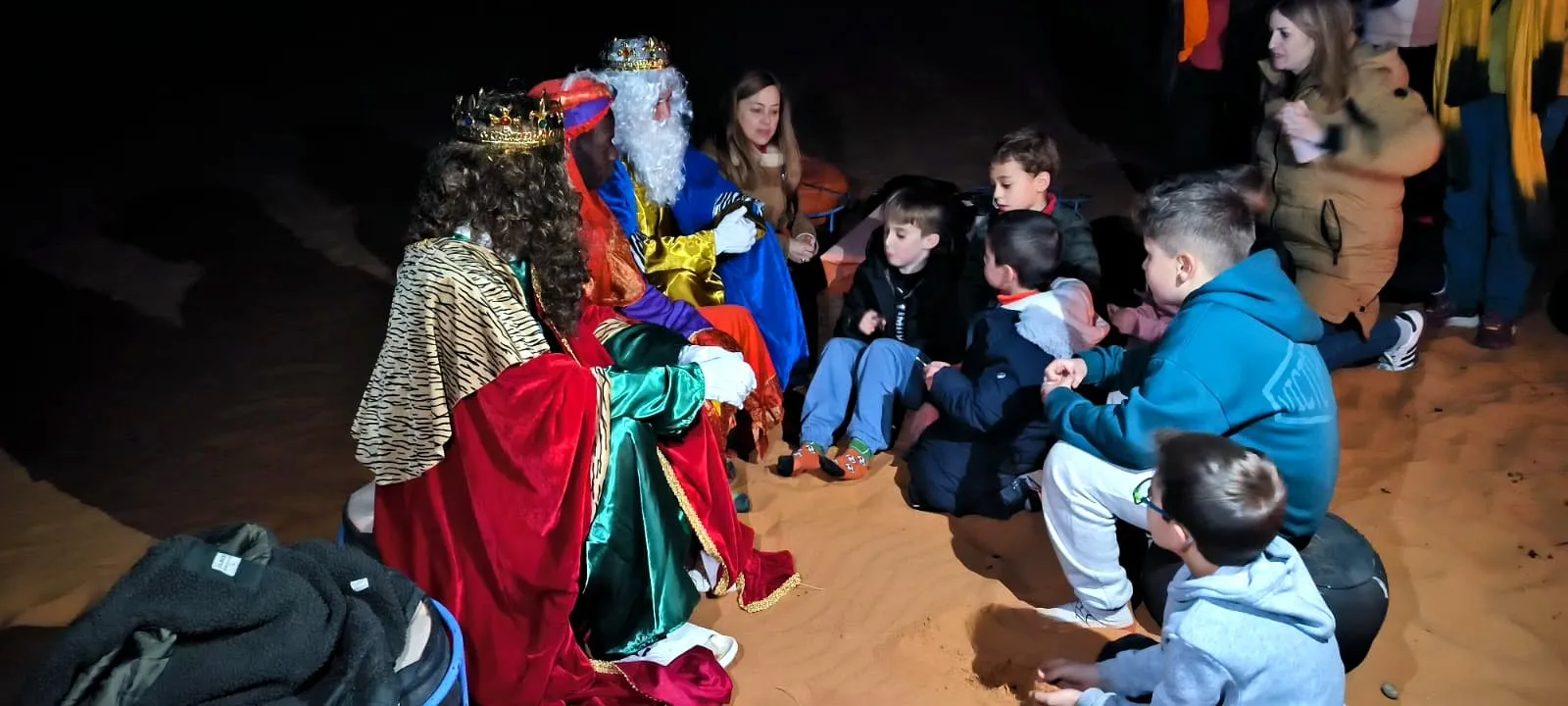Los niños sentados alrededor de los Reyes Magos en el campamento, en el viaje de otro año