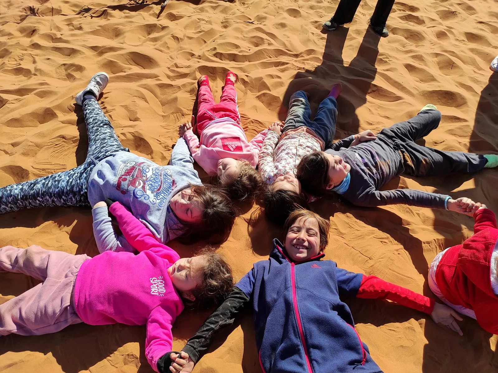 Niños tumbados en la arena del desierto formando una estrella, en uno de nuestros viajes de Reyes